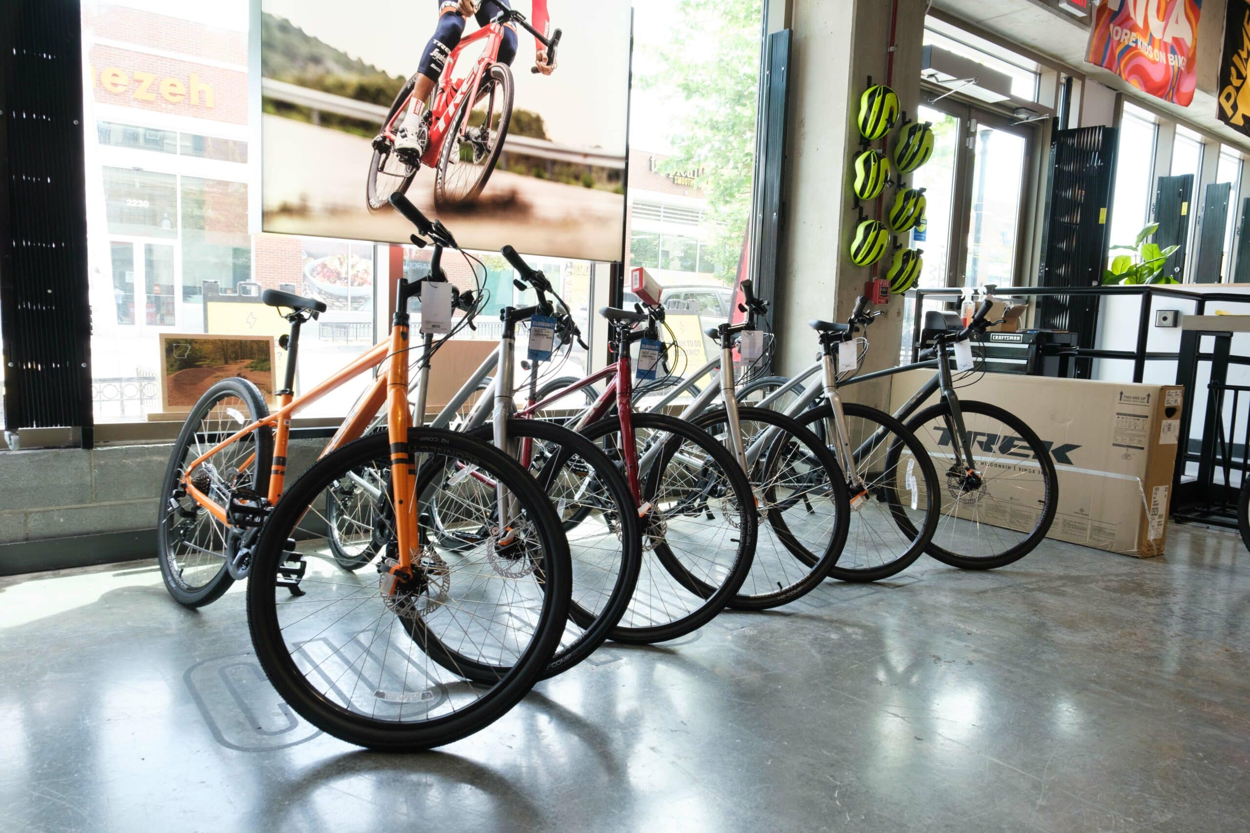 Bicycles on display in a shop, with a window showcasing a cyclist in motion. Helmets are mounted on a rack.