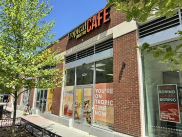 Exterior view of a Tropical Smoothie Cafe with vibrant signage and promotional posters on the windows.