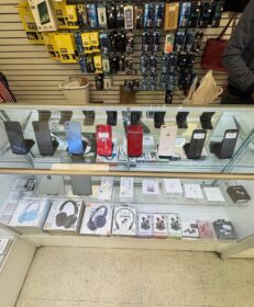 A glass display case with smartphones on top and various headphones and earphones inside, in a DC Phone Repair store with accessories hanging on the wall behind.